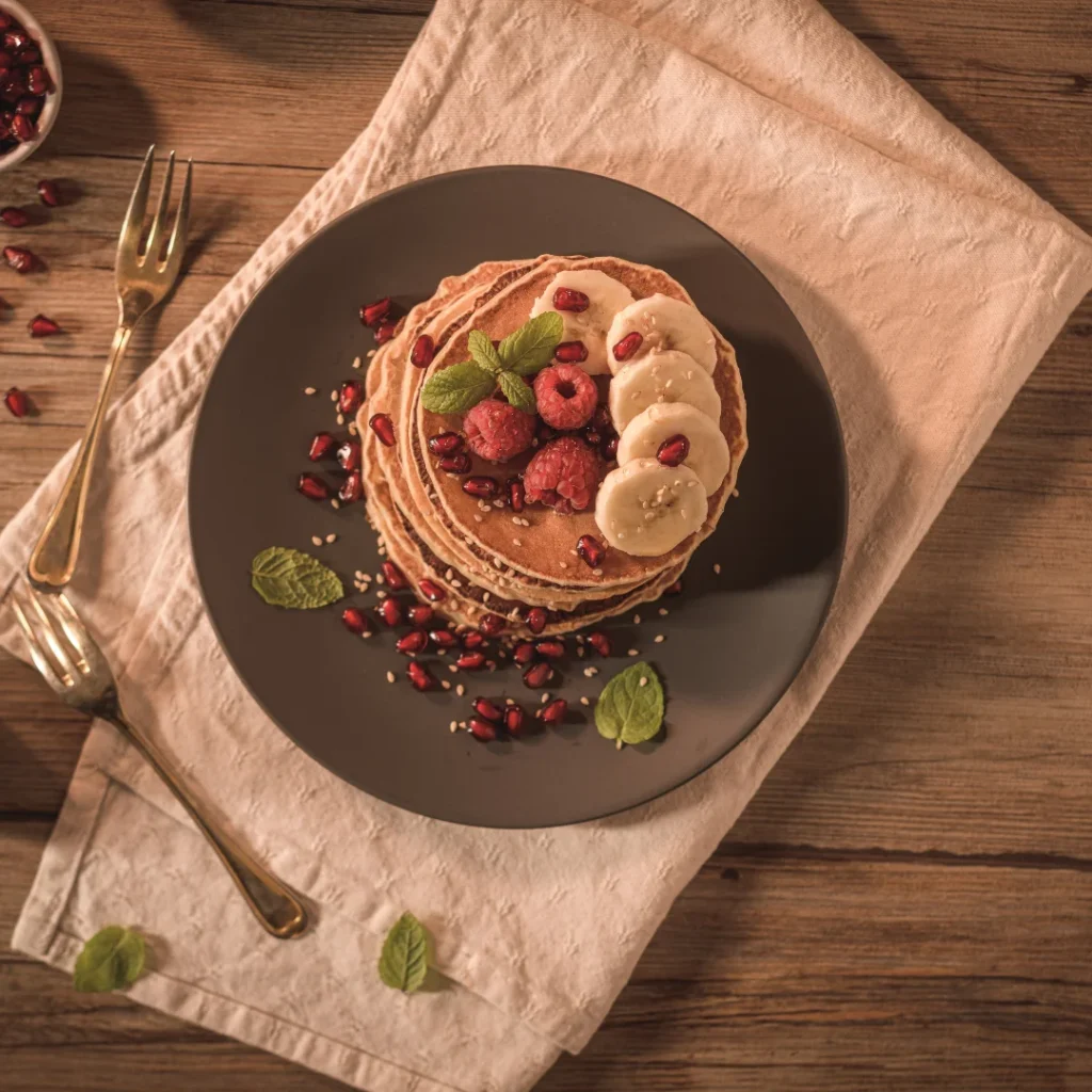 Uma pilha de panquecas americanas douradas dispostas em um prato, decoradas com rodelas de banana fresca e sementes de linhaça polvilhadas